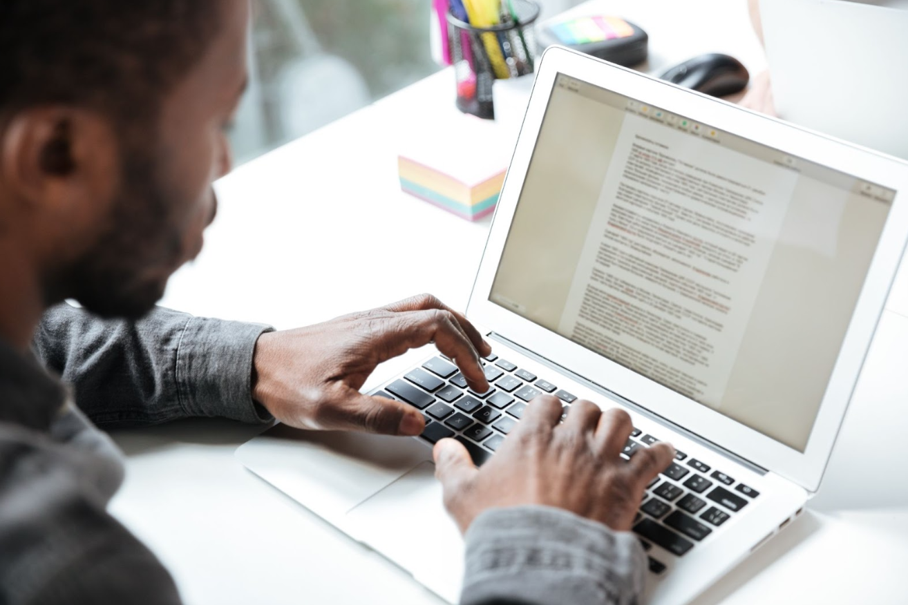 Homem trabalhando em um laptop enquanto edita um documento de texto. Criar conteúdo relevante e de qualidade é um dos pilares de o que é marketing digital, ajudando a atrair e engajar audiência por meio de blogs, e-books e artigos.