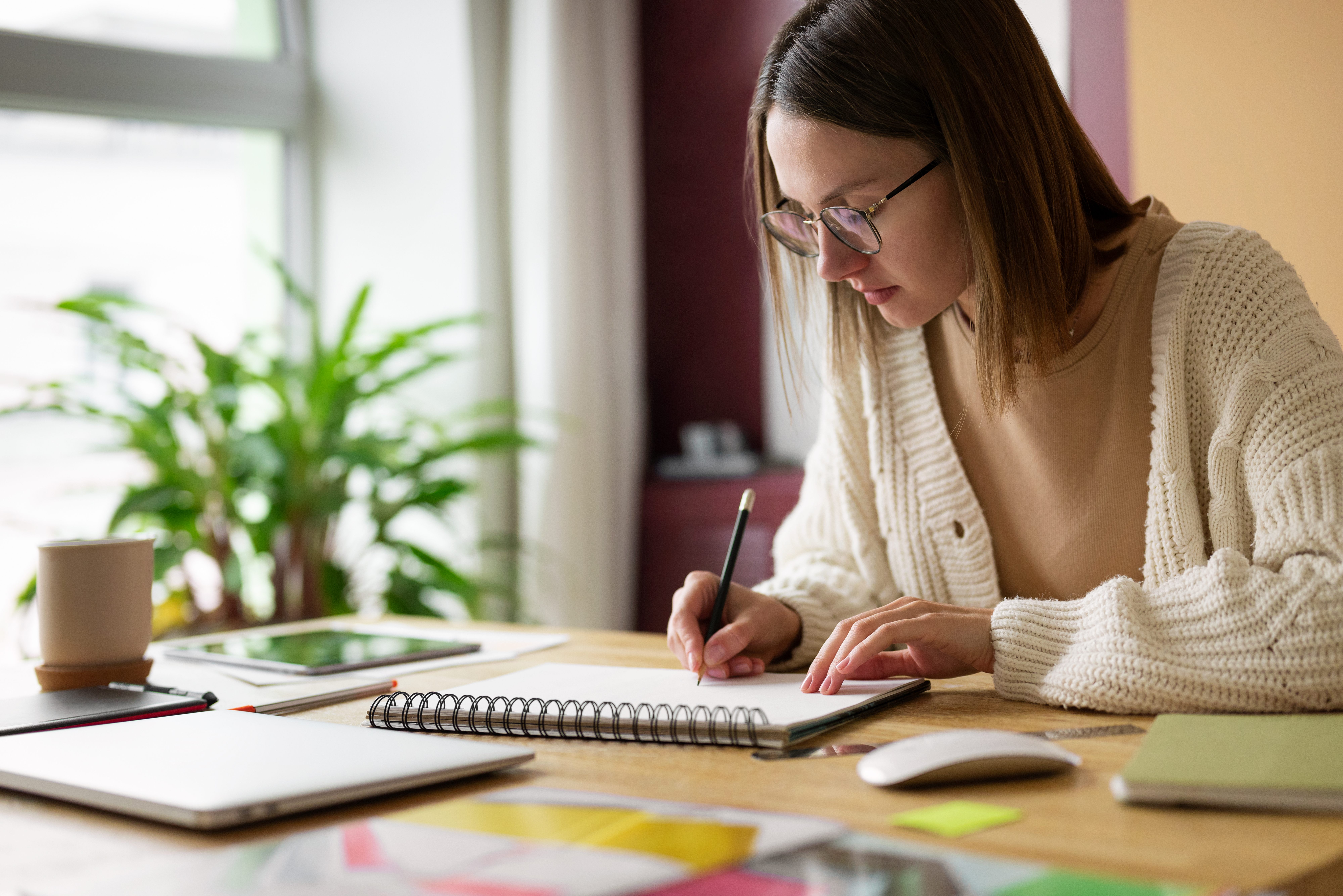 Jovem concentrada estudando em casa, escrevendo em caderno sobre uma mesa organizada, com a palavra-chave estudar.