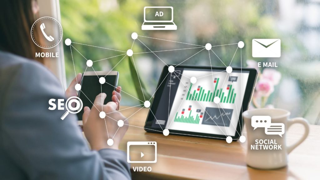 Profissionais diversos usando smartphones em fila, com ilustrações de ícones ligados ao marketing digital ao fundo.