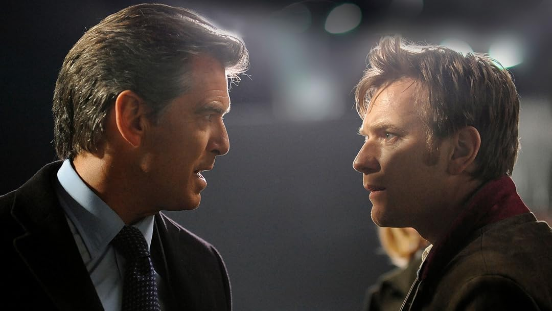 Uma imagem aproximada de dois homens, Pierce Brosnan e Ewan McGregor (atores do filme "O Escritor Fantasma"), olhando um para o outro com intensidade. Brosnan, à esquerda, veste um terno e gravata e tem uma expressão séria, enquanto McGregor, à direita, usa uma jaqueta mais casual e parece pensativo. Esta cena captura a interação central entre um político e seu Ghost Writer, sugerindo intriga e revelações.