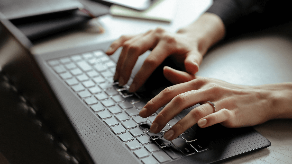 Jovem digitando em notebook em ambiente de trabalho moderno com pôsteres sobre estratégias de marketing digital nas paredes.