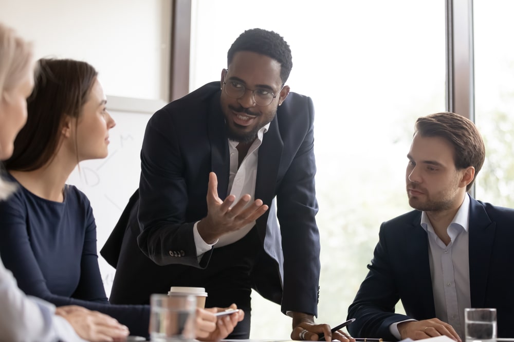Profissional em traje formal se comunicando com uma equipe durante uma reunião, ilustrando um momento estratégico de brainstorming ou apresentação de ideias, simbolizando a criação colaborativa de textos persuasivos no contexto de copywriting.