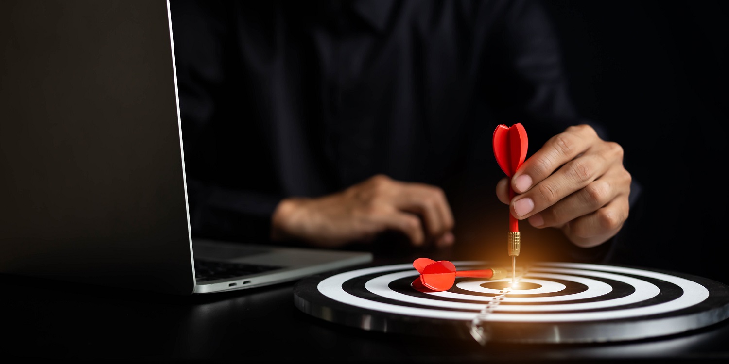 Profissional segurando um dardo vermelho acertando o centro de um alvo ao lado de um notebook, simbolizando foco, precisão e estratégia no processo de conversão de leads dentro do funil de vendas.