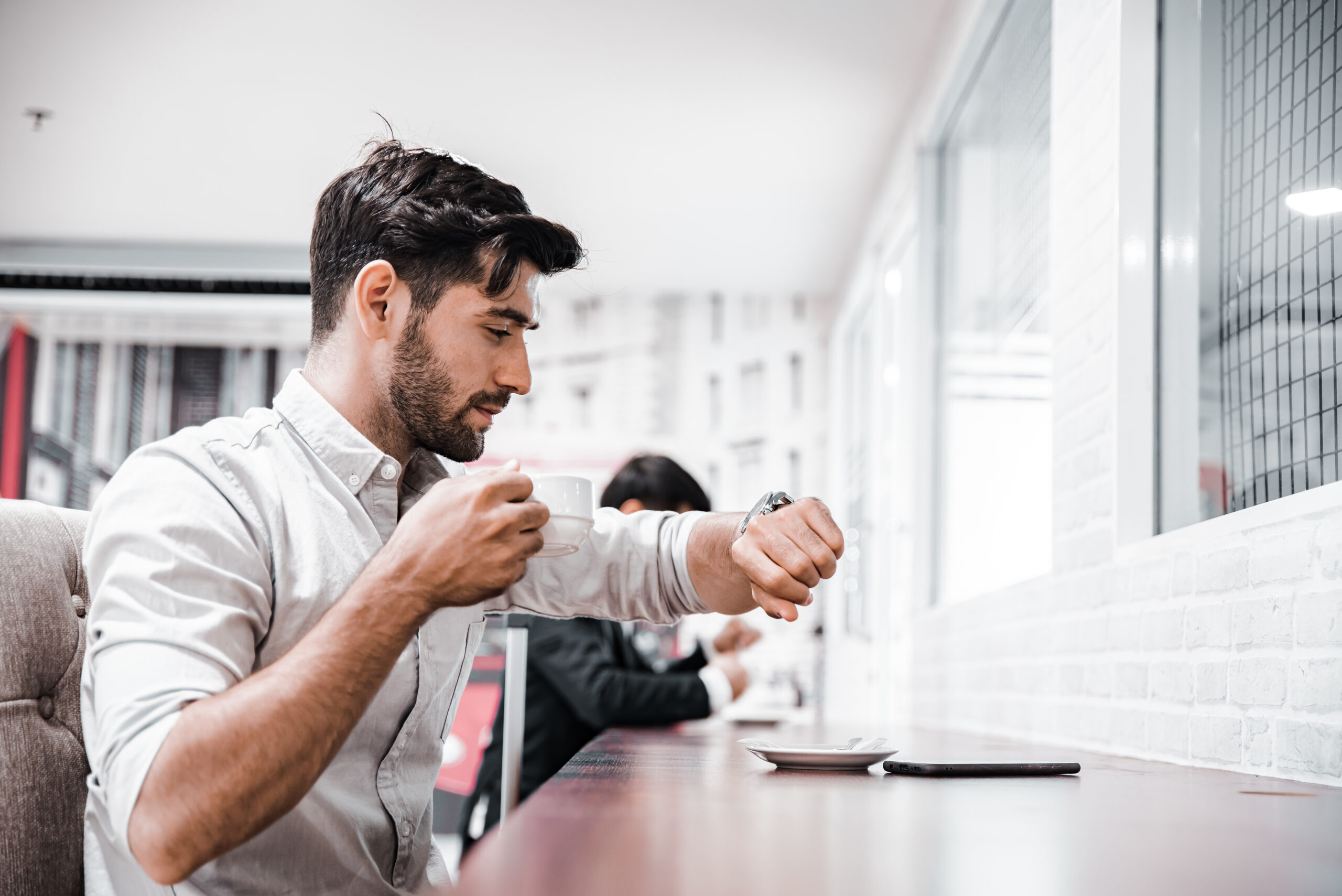 Homem tomando café e verificando o horário, se organizando para estudar em um ambiente tranquilo e confortável.