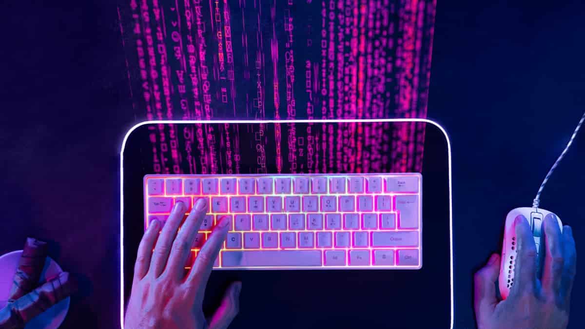 Uma pessoa digitando em um teclado gamer iluminado, com código binário em rosa e roxo projetado na parede. A imagem representa o uso de tecnologia e estratégias digitais para aumentar o "Alcance no Instagram".