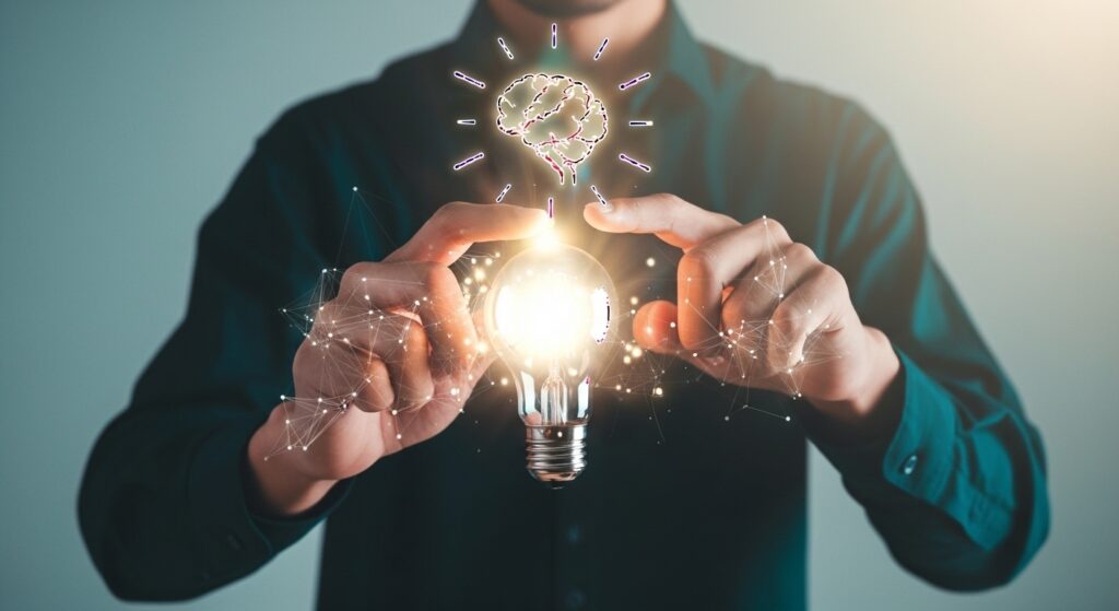 Um homem segura uma lâmpada acesa com as pontas dos dedos, simbolizando uma nova ideia ou solução. Acima da lâmpada, uma representação gráfica de um cérebro com as laterais conectadas à lâmpada por linhas de luz. O foco da imagem está na lâmpada e nas mãos do homem, com as laterais da imagem desfocadas. A cena é uma representação visual do processo criativo para o desenvolvimento de Criativos de Produtos Digitais.