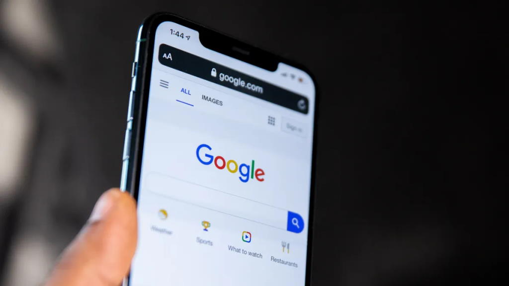 Um close-up de uma mão segurando um smartphone com a página inicial do Google aberta. A imagem ressalta a relevância do SEO Técnico para garantir que sites e conteúdos sejam otimizados para dispositivos móveis, proporcionando uma boa experiência de navegação e uma performance de pesquisa eficiente.
